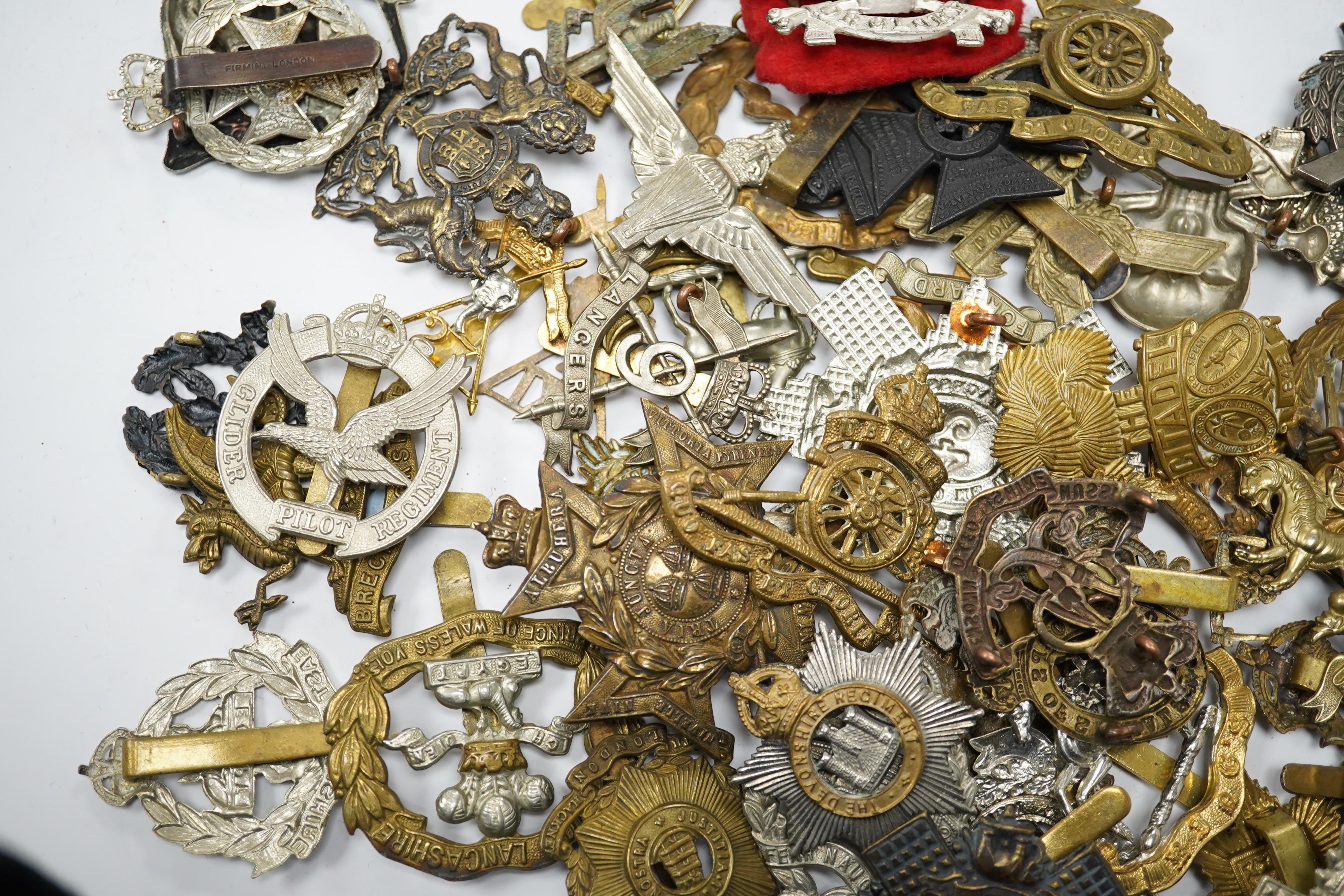 Sixty military cap badges, including; the Brecknockshire Regiment, the Royal Warwickshire Regiment, the South Lancashire Prince of Wales Volunteers, the Royal Artillery, the East Lancashire Regiment, the Glider Pilot Reg